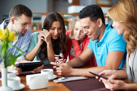 Two young men and two young woman all looking at one of their cell phones and smiling