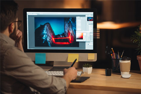 Bearded man with glasses designing with a stylus and a computer monitor with a design program